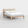 A minimalist wooden bed frame with light-colored wood, a beige upholstered headboard, and white bedding with two pillows, set against a plain white background.