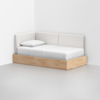 A minimalist daybed with light wood frame and white cushioned backrests is positioned in the corner of a white room, featuring a single pillow and neatly made white bedding.