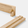 Two light wood bed frame pieces with precise interlocking joints are shown on a white background, illustrating a minimalist, tool-free assembly method.