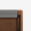 Close-up of the corner of a wooden crib with rounded edges and a gray fabric or felt panel attached to the top rail.