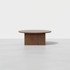 A round wooden coffee table with a simple, flat top and a solid rectangular base, set against a plain white background.