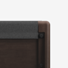 A close-up of the corner of a dark wooden bed frame with a soft, gray fabric headboard panel, showing smooth rounded edges and visible hardware.