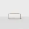 A minimalist, rectangular wooden table or bench with open sides, placed on a light gray, textured surface against a plain white background.