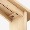 Close-up view of a wooden table’s underside, showing the corner joint where the tabletop meets the leg, with visible screws and a natural wood finish.