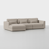 A modern, light beige sectional sofa with a left-facing chaise, three seat cushions, three back cushions, and three rectangular lumbar pillows, set against a plain white background.