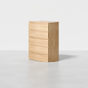 A light wood, five-drawer dresser with a minimalist design, standing on a smooth, light gray floor against a plain white background.
