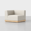 A modern, minimalist corner armchair with light beige upholstery and a low wooden base, set against a plain white background.
