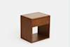 A modern wooden nightstand with a rectangular shape, featuring an open lower shelf and a single drawer. The top surface appears to be a lighter color, possibly cushioned or textured. The background is plain white.