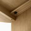 Close-up view of the underside of a wooden table showing a corner joint, a black screw, and smooth, light wood grain with precise craftsmanship. The angle highlights the table’s detailed construction.