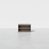 A small, rectangular wooden shelf with an open front and two compartments, placed on a plain, light gray floor against a white background.