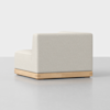 A modern, armless, beige upholstered chair with clean lines sits on a light wooden base against a plain white background.