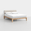 A modern bed with a light wood frame, light beige upholstered headboard, white bedding, and two pillows, set against a plain white wall and floor in a minimalistic room.