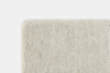 Close-up view of the corner of a textured, off-white carpet or rug with a soft, looped pile against a plain white background.