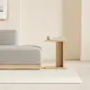 A minimalist wooden bed with white bedding is positioned next to a small, light wood nightstand against a plain white wall and light gray floor.