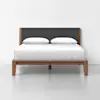 A modern wooden bed frame with a dark upholstered headboard, white bedding, and two white pillows, set against a plain white wall and floor.