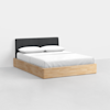 A modern bed with a light wooden frame, a dark upholstered headboard, and white bedding with two pillows, set against a plain white wall and floor.