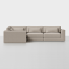 A modern, light beige L-shaped sectional sofa with low arms and three seat cushions, set against a plain white background. Two matching rectangular throw pillows rest on the sofa.