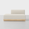 A modern, minimalist armless sofa with a low backrest, upholstered in light beige fabric, and a simple wooden base, set against a plain light background.