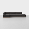 A modern, dark gray sectional sofa with a low profile and clean lines sits on a light-colored floor against a plain white background. The sofa has a left armrest and an open right end.