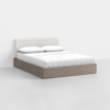 A modern bed with a light wood frame, white cushioned headboard, and white bedding with two pillows, placed in a minimalistic room with a light gray floor and white walls.