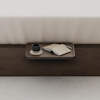 A wooden tray on a dark wooden surface holds a cup on a saucer, an open notebook, and a pen, placed at the foot of a neatly made bed with a cream-colored blanket.