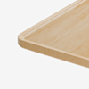 A close-up view of the corner of a rectangular, light-colored wooden tray with smooth, rounded edges on a white background.
