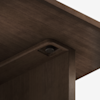 Close-up view of the underside of a wooden table showing a metal fastener or connector securing the tabletop to the leg structure. The wood has a smooth, dark brown finish.