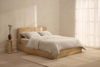 Two beige pillows are stacked on top of a neatly folded beige comforter, all against a plain white background.