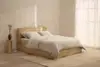 Two beige pillows are stacked on top of a neatly folded beige comforter, all against a plain white background.