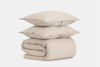 Two beige pillows are stacked on top of a neatly folded beige comforter, all against a plain white background.
