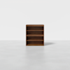 A medium-height wooden bookshelf with three shelves is standing on a smooth, light gray floor against a plain white background.