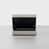 A beige upholstered storage ottoman with the lid open, revealing a spacious black interior, is placed on a light gray floor against a plain white background.
