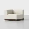 A modern, cream-colored upholstered corner chair with clean lines, a low backrest, and a dark wooden base, set against a plain light gray background.
