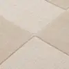 A close-up of a textured carpet with a geometric pattern of large, alternating light beige and off-white squares forming a diagonal grid.
