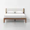 A modern wooden bed frame with a light beige upholstered headboard, neatly made with white bedding and two pillows, set against a plain white wall and floor.