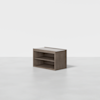 A small, rectangular wooden shelf unit with two open shelves, placed on a plain, light gray floor against a white background.