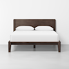 A dark wooden bed frame with a high headboard, neatly made with a white sheet and two white pillows, set against a plain white wall and a light-colored floor.