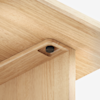 A close-up of the corner joint of a light wood table, showing precise craftsmanship and a visible black screw embedded neatly into the recessed joint.