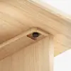 A close-up of the corner joint of a light wood table, showing precise craftsmanship and a visible black screw embedded neatly into the recessed joint.