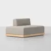A modern, minimalist loveseat with light gray upholstery, a low backrest, and a light wooden base, set on a smooth, light gray floor against a plain white background.