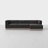 A modern, dark gray L-shaped sectional sofa with low backrests and wooden base, placed in a minimalistic, light-colored room.