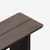 A close-up view of the corner of a modern wooden table with a dark brown finish, featuring a split down the center and rounded edges, set against a plain white background.