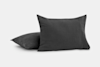Two dark gray square pillows with a soft, textured fabric, one standing upright and the other lying flat on a plain light background.