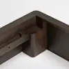 Close-up of a dark wood furniture joint showing the corner connection of two panels, with smooth rounded edges and precise assembly against a white background.