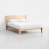 A minimalist wooden bed frame with a matching headboard, dressed in white bedding and two white pillows, set against a plain white wall and light gray floor.