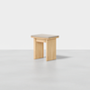A minimalist wooden stool with a square, light-colored seat and four sturdy legs, set against a plain white background.