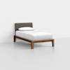 A minimalist single bed with a wooden frame, white bedding, a single pillow, and a dark upholstered headboard, placed in a plain, light-colored room.