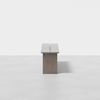 Minimalist wooden bench photographed from the end against a plain white background, showing a simple, rectangular design with a visible vertical gap down the center of the seat.