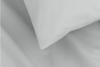 A close-up view of a white pillow resting on a white bed sheet, highlighting the smooth and clean fabric.