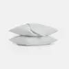 Two white pillows are stacked with a folded white sheet draped over the top pillow, all set against a plain white background.